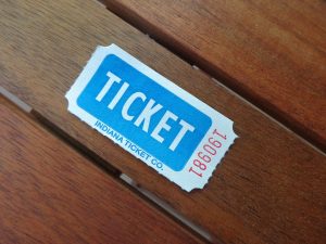 Blue and white paper ticket labeled "ticket for College Education" placed on a wooden surface.