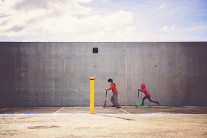 Two children ride scooters in a concrete urban space under a partly cloudy sky, symbolizing the ongoing report on measuring opportunities for working families.