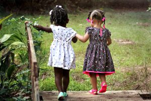 Two young girls holding hands, walking on a wooden path outdoors, captured in an infographic on the high cost of child care.