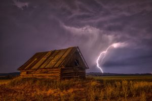 Lightning strike near a dilapidated wooden cabin in Colorado at night.