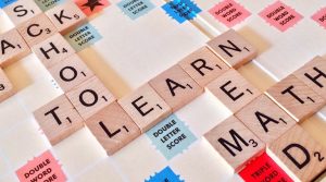 Scrabble tiles spelling out "school," "learn," and "math" on a game board for a Colorado equivalency assessment.