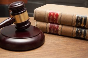 A gavel resting on its sound block beside a stack of legal books related to HB16-1299 on a wooden surface.