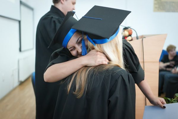 Two graduates in caps and gowns, benefiting from the Middle Class College Savings Act, embracing at a graduation ceremony.