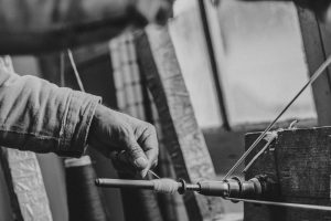 A person's hand operating a traditional spinning wheel to twist fiber into yarn as part of an Apprenticeship Study.