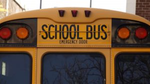 Rear view of a yellow school bus with an 'emergency door' sign, labeled for SB17-118 compliance, emphasizing greater transparency in private occupational schools.