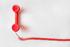 Red telephone handset with coiled cord on a white background, serving as a testimony to the Colorado Fair Debt Collection Practices Act.