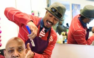 Barber applying product to a client's hair in a salon with a mirror reflecting his image, fueled by big dreams and small loans.