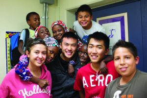 A diverse group of smiling students gathered in a school hallway with their teacher, standing as a bridge to opportunity.