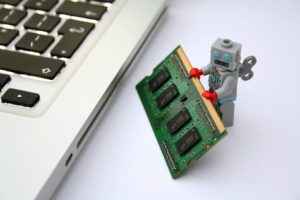 A toy robot holding a ram module stands next to a laptop computer, showcasing what to know about technology integration.