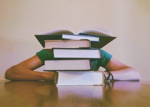Person resting head on table surrounded by a stack of books, overwhelmed by high student debt from attending a for-profit college.
