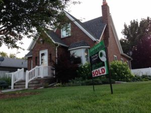 A brick house with a sold sign on the front lawn, symbolizing homeownership hopes amidst student debt.