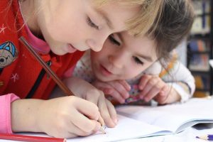 Two children concentrating on writing in a notebook as part of an early insights pilot program.