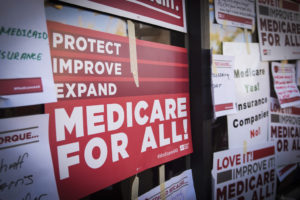 Signs advocating for the expansion and improvement of Medicaid work requirements for all displayed on a window.
