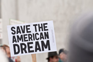 Protest sign reading "save the American dream, ensure economic mobility in Colorado" held aloft in a crowd.