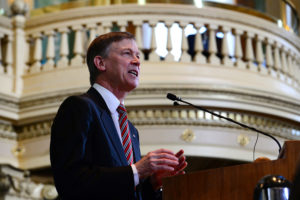 A man in a suit with a striped tie speaking at a podium in a legislative chamber about two-generation strategies.