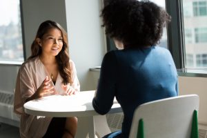 Two individuals engaged in a conversation about compensation information practices at a table inside a room with natural light.