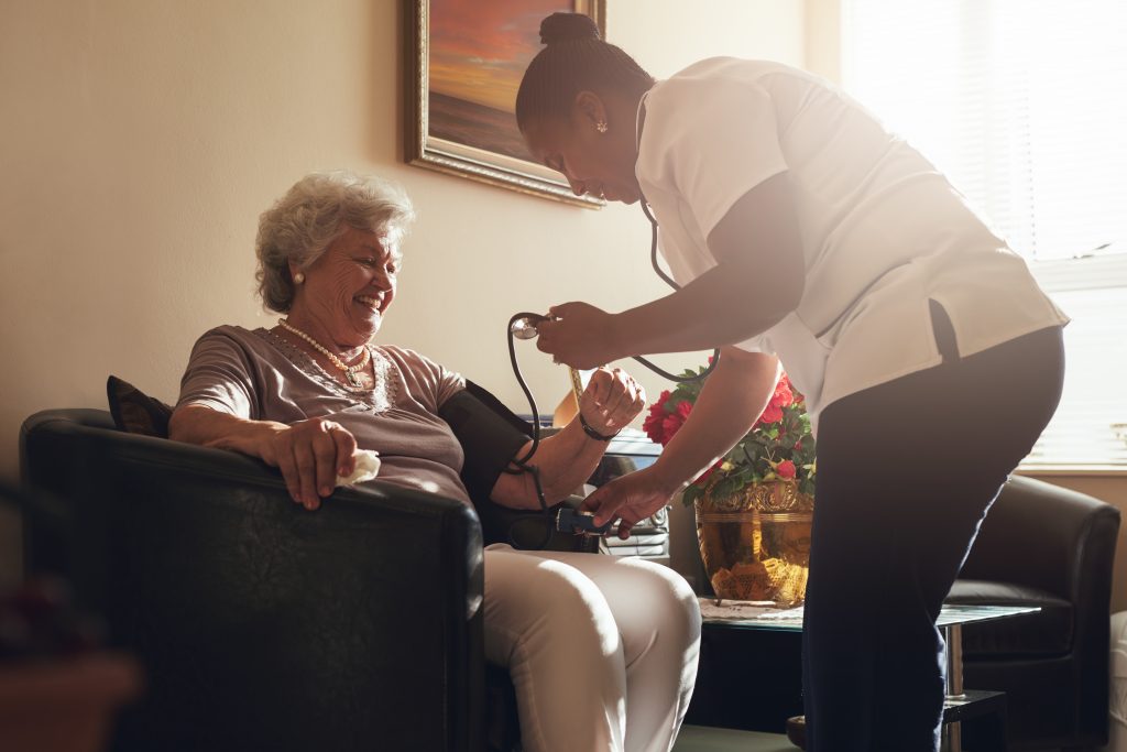 A healthcare professional checks the blood pressure of an elderly woman in a home setting, as part of a Senior Care program.
