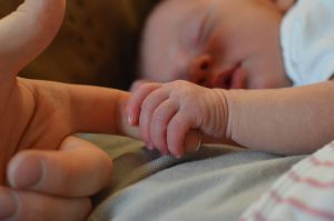 A newborn baby holding an adult's finger while sleeping, a moment captured from a real story.