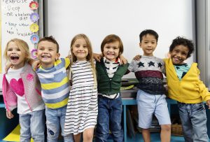 A group of diverse, happy children standing in front of a whiteboard in an affordable child care setting in Colorado.