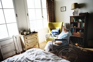 An elderly person sitting in a wheelchair by a window in a cozy room, evidencing the roadmap of Aging in Colorado.