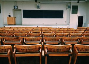 An empty university lecture hall with rows of wooden seats and a blackboard at the front, often filled with students eager for higher education.