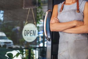 Shop owner standing by the entrance with a "portable benefits" open sign.