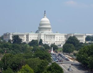 The United States Capitol building, a backdrop to numerous political issues, viewed from an elevated angle with trees and street traffic in the foreground.