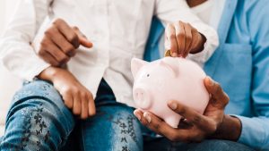 Two people in Colorado sitting together, inserting coins into a pink piggy bank, discussing the updated data on the retirement crisis.