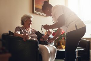 Healthcare professional from the direct care workforce taking an elderly woman's blood pressure in a home setting in Colorado.
