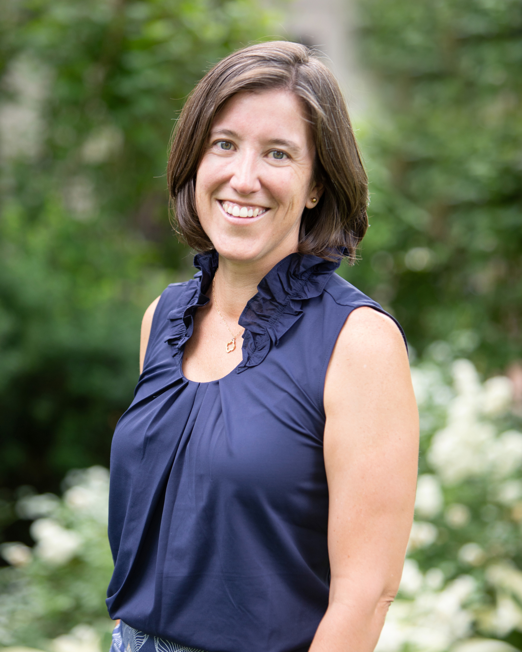 Woman smiling outdoors with greenery in the background after a refreshing board meeting.