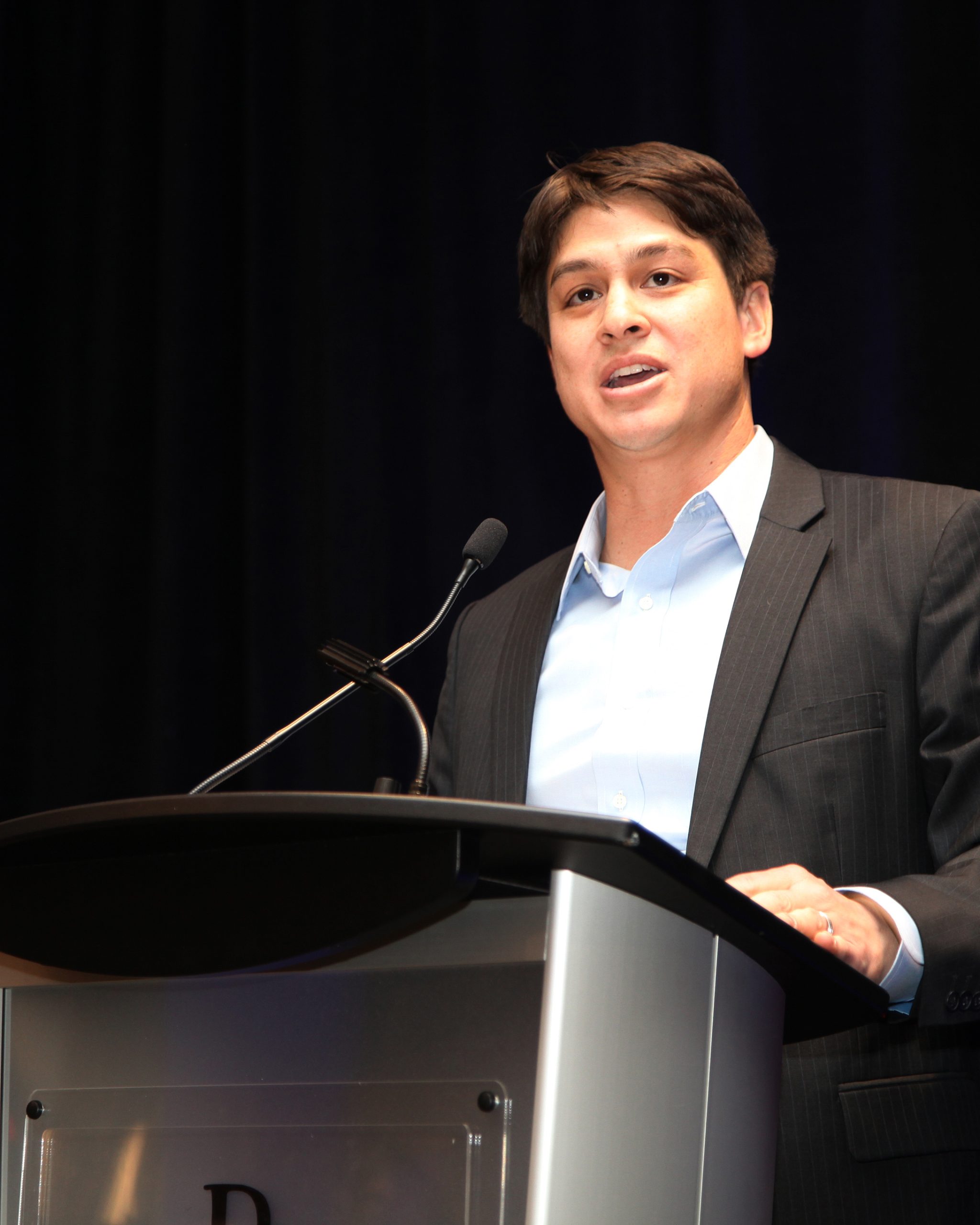 A man speaking at a podium in front of a board.