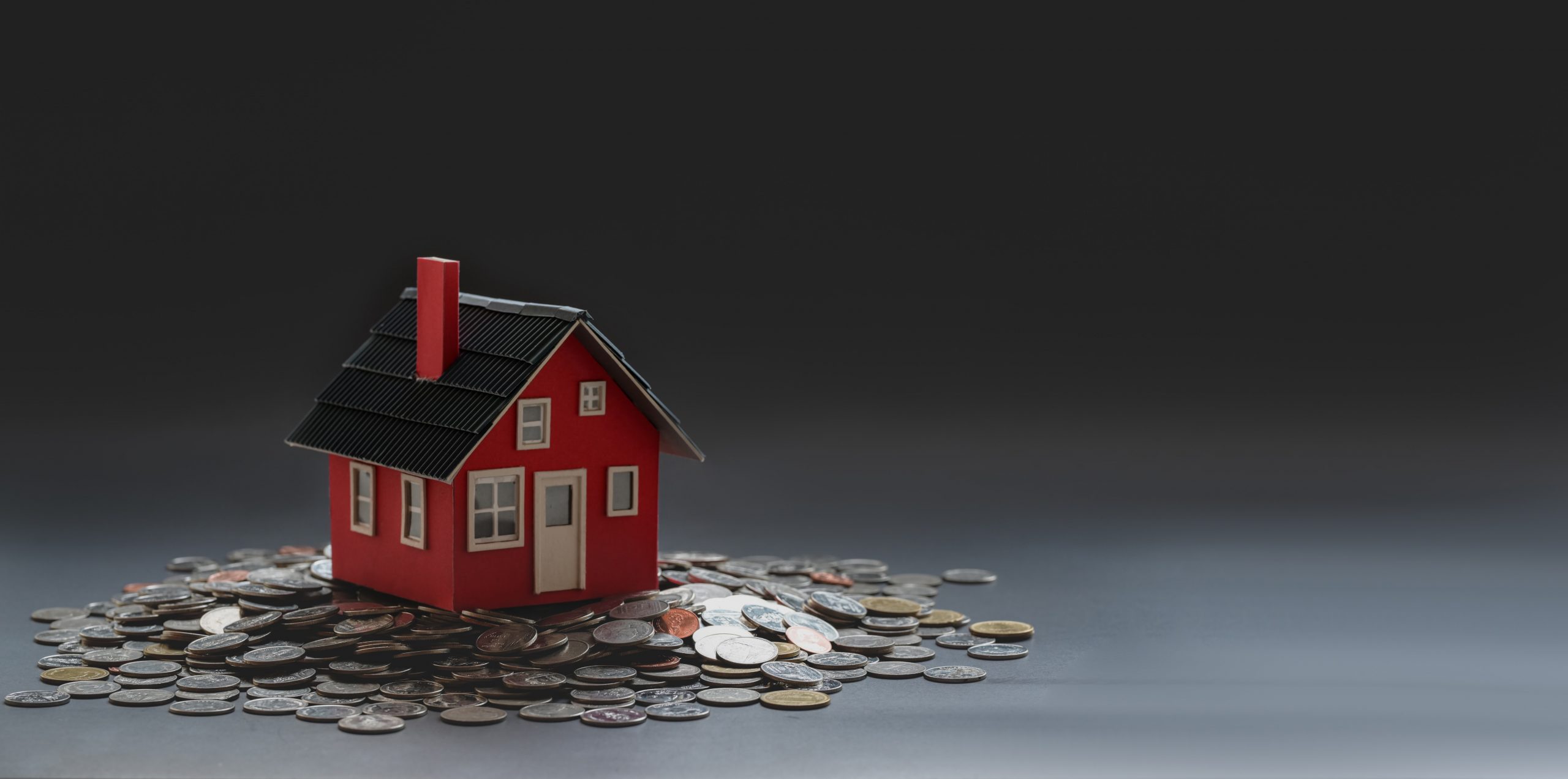 Miniature red house surrounded by coins on a gray background, amendment b.