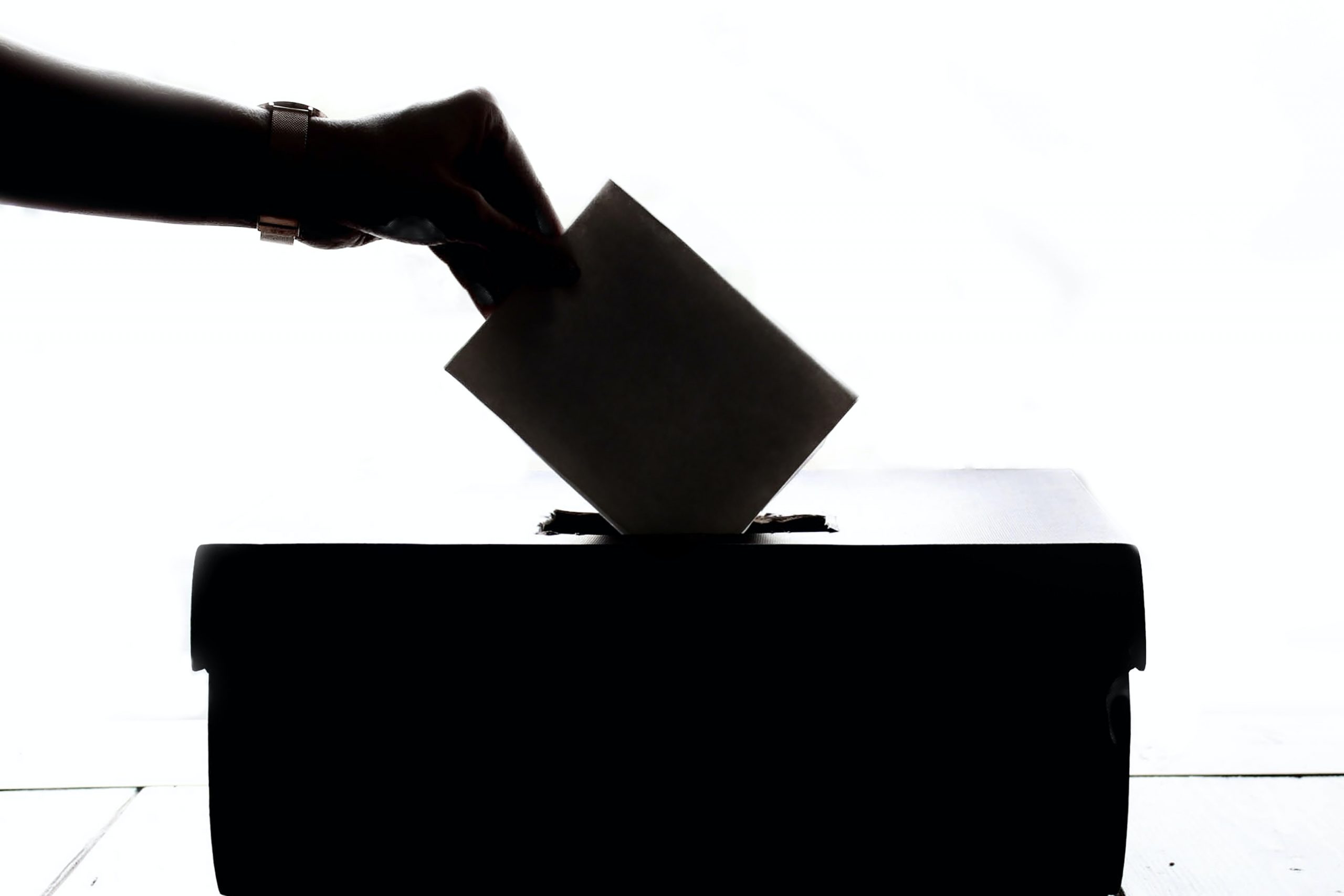 Silhouetted hand casting a Colorado ballot into a voting box, keeping an eye on democracy.
