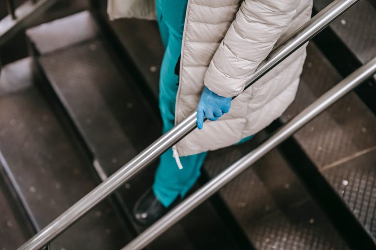 Person wearing a coat and gloves, representing Colorado's caring workforce, holding onto an escalator handrail.