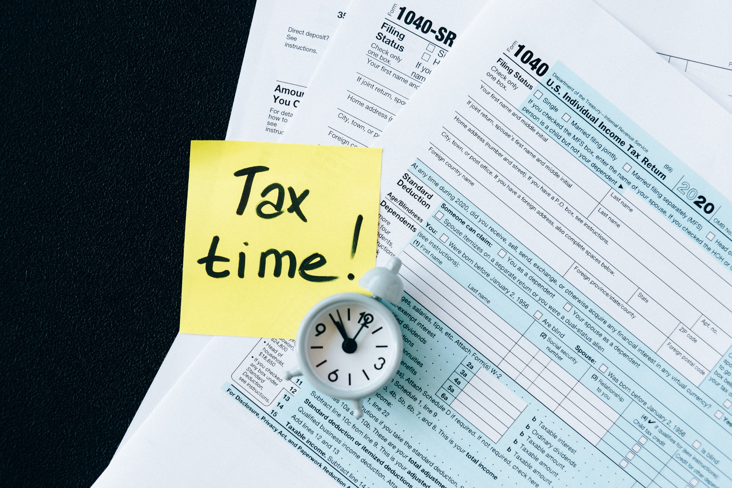 A clock on top of tax forms with a sticky note stating "Tax Time! What's Inside the New Tax Reform Package?
