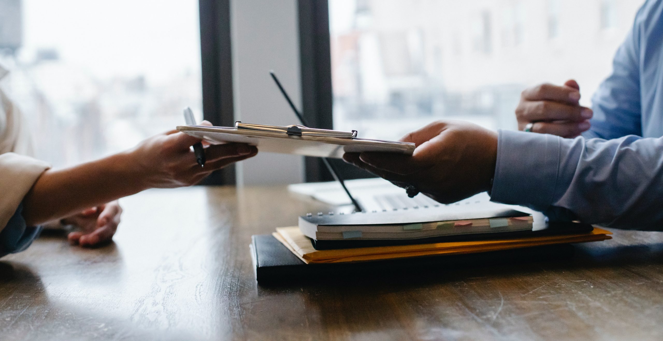 Two individuals in Colorado at a table, one passing a clipboard to another for review or signature.