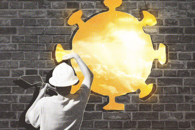 A person painting a glowing representation of the COVID virus on a brick wall.