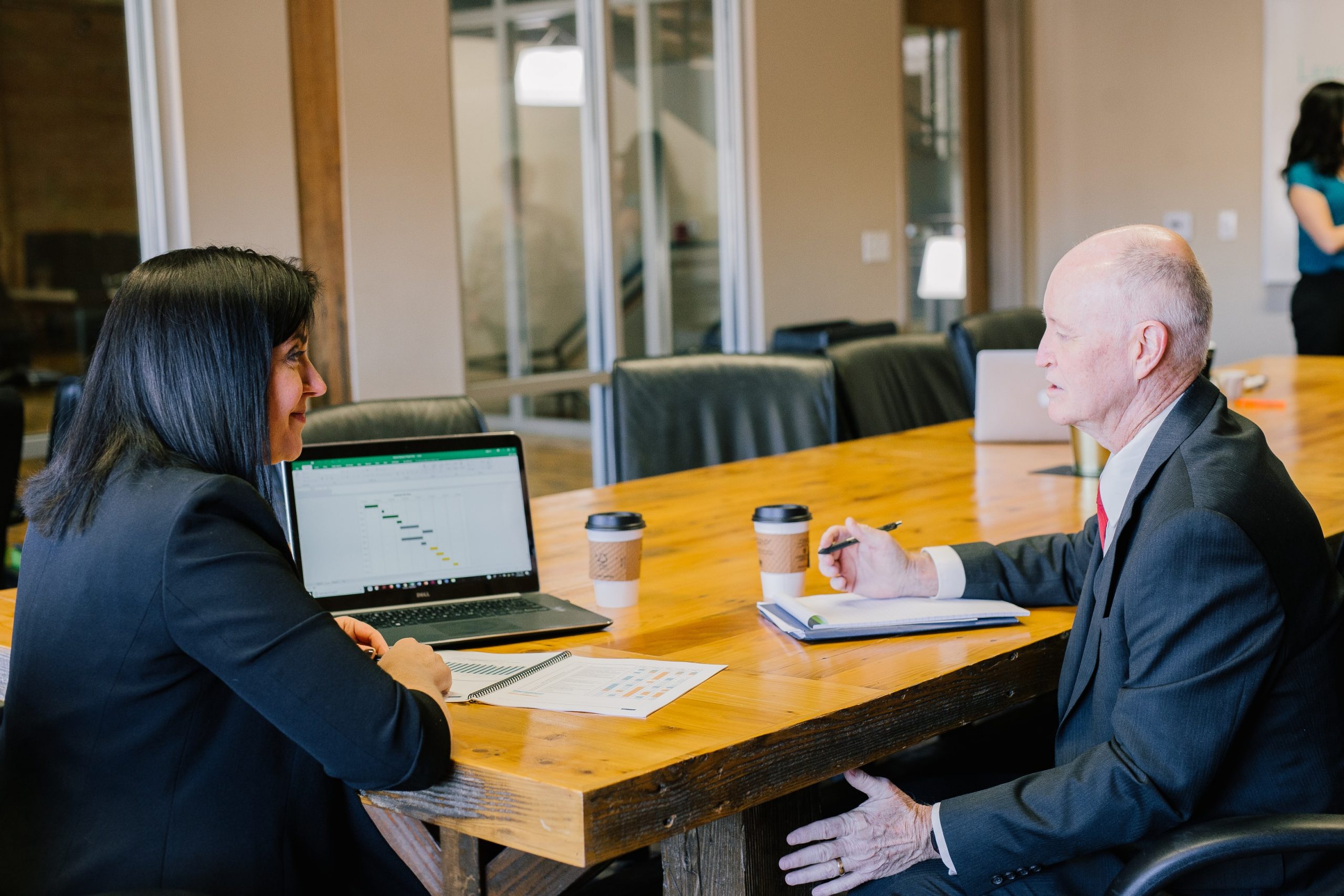 Two professionals in a meeting with laptops and documents on a wooden table, discussing economic insecurity.